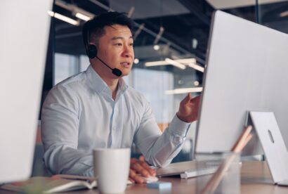 Focused asian businessman in headphones talking online with client sitting in office