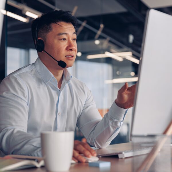 Focused asian businessman in headphones talking online with client sitting in office