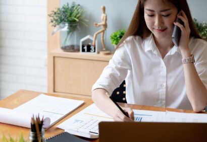 Smiling asian woman taking call on mobile phone during working on laptop computer for financial